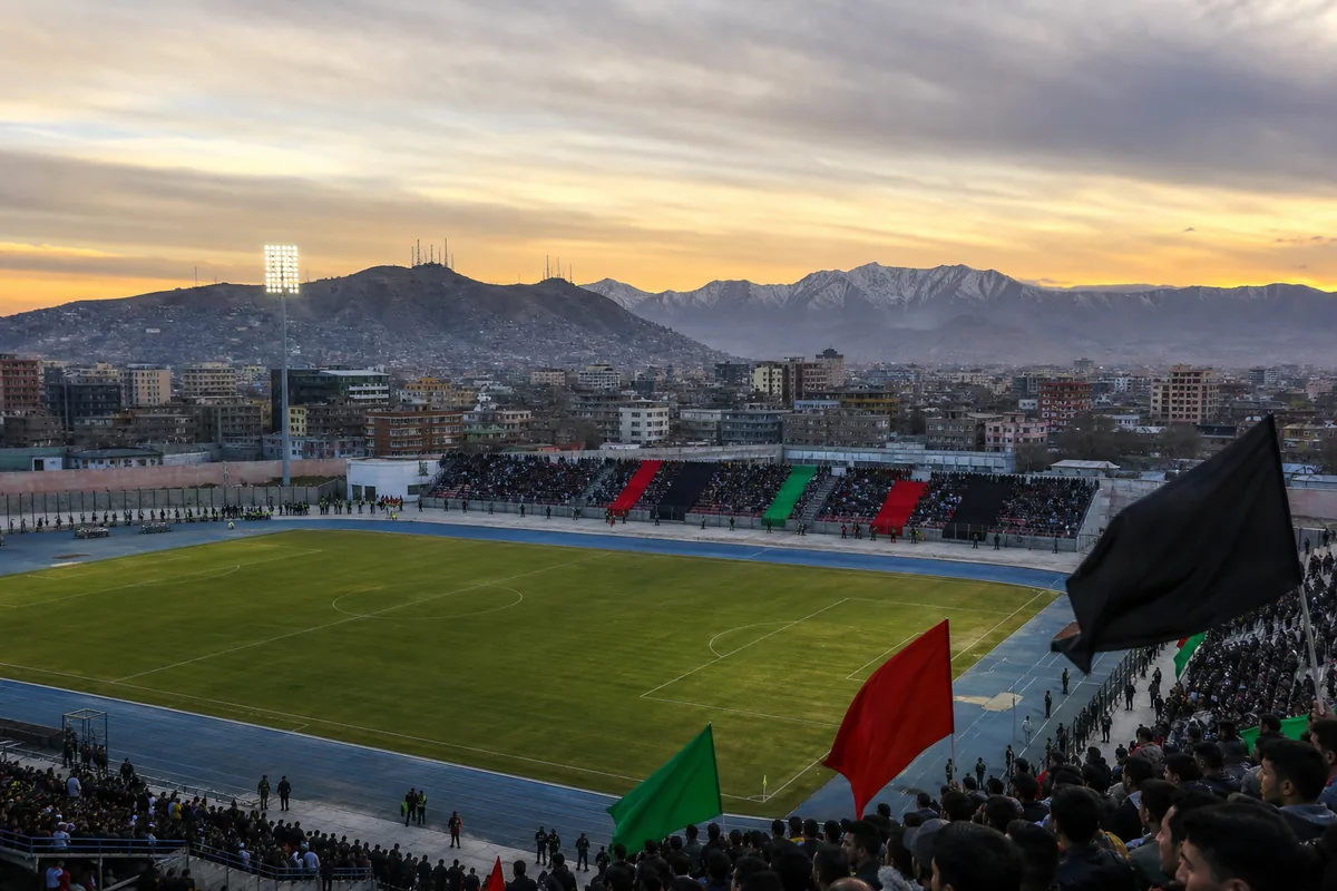A compact Afghanistan football stadium in a Kabul-inspired mountain setting prepared for an international match