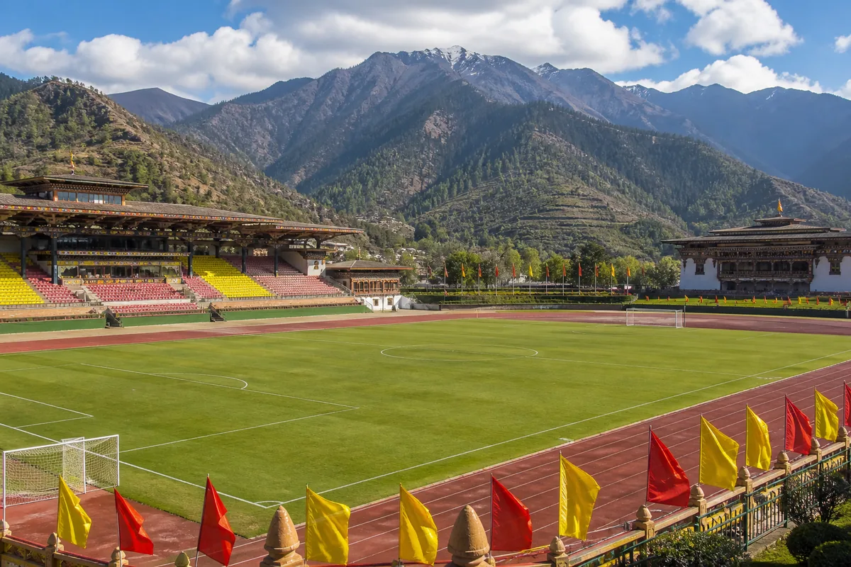 A Changlimithang Stadium-inspired football ground in Thimphu with Himalayan mountains behind the stands