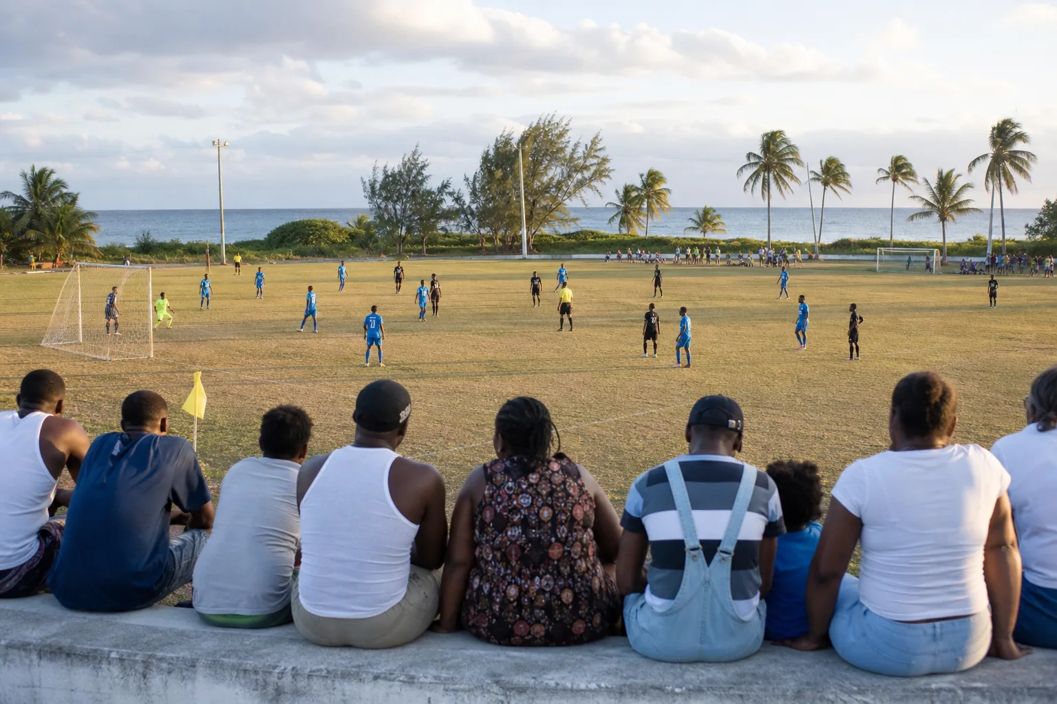 A community football match on a Cayman Islands pitch with blue-shirted players and island supporters