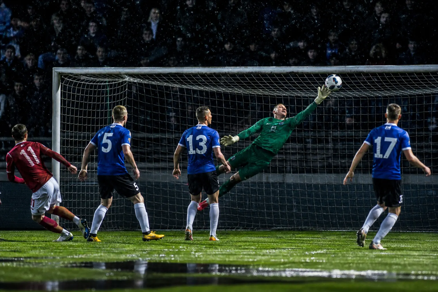 A fictional Estonian goalkeeper making a one-handed save in a tense European qualifier