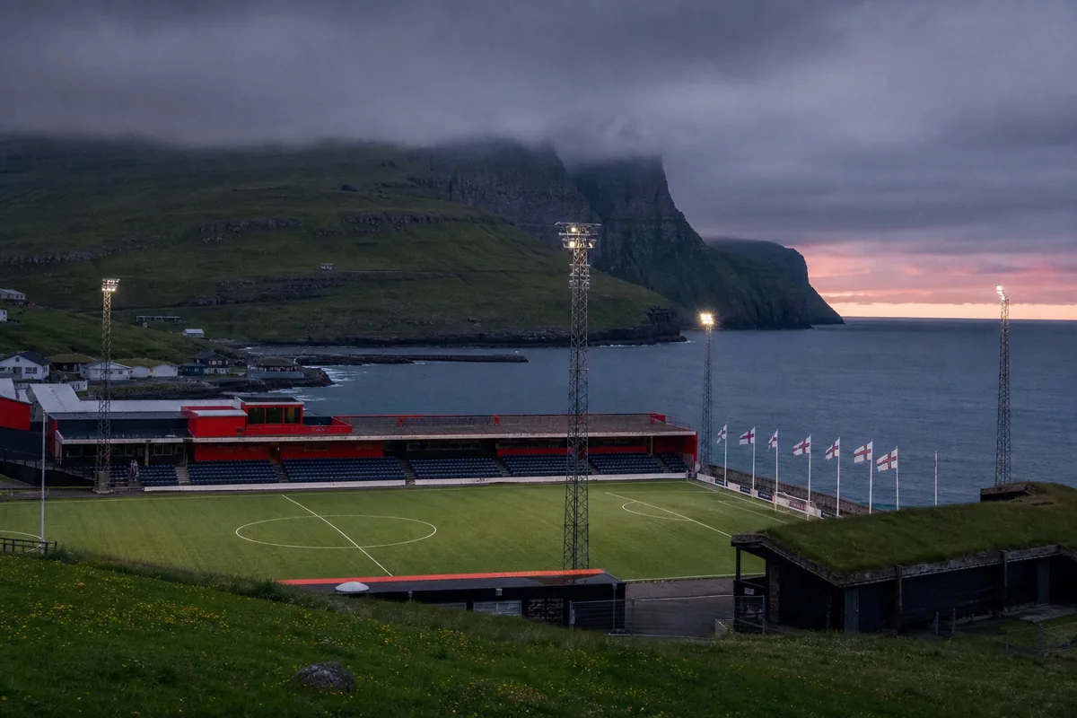 A Faroese football stadium beside the ocean and steep green cliffs under low evening cloud
