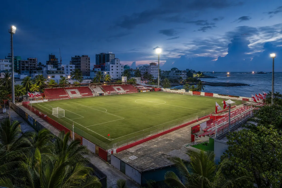 A compact Malé football stadium-inspired ground prepared for a South Asian match among tropical palms