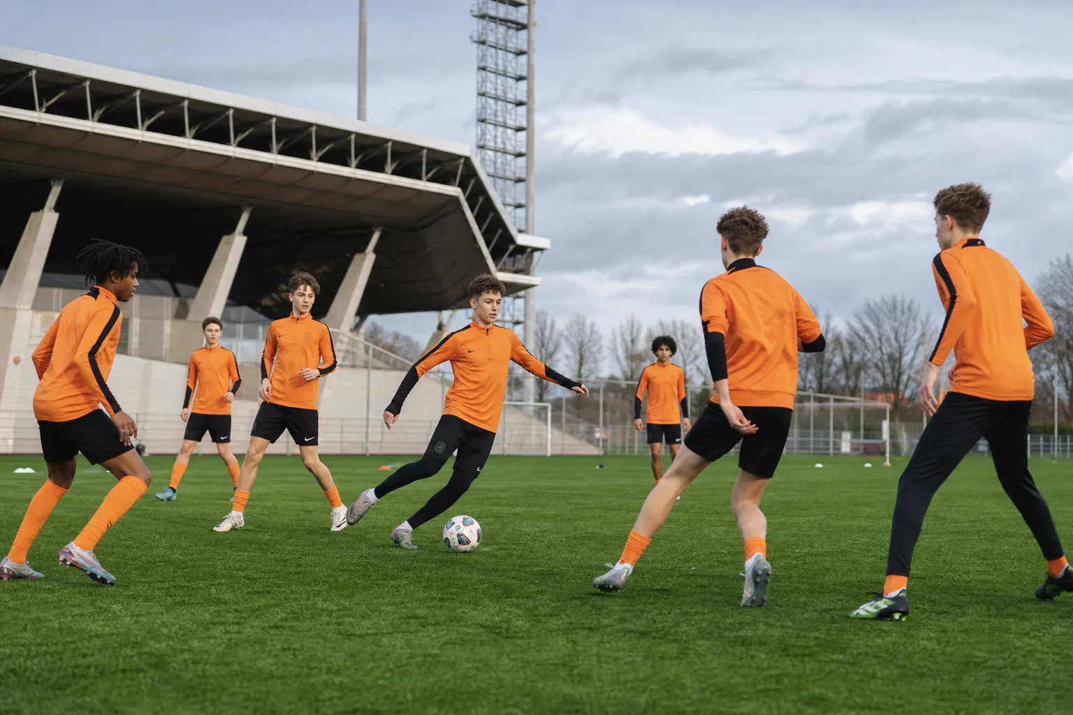 Fictional Dutch youth players moving through a coordinated passing drill on a green training pitch