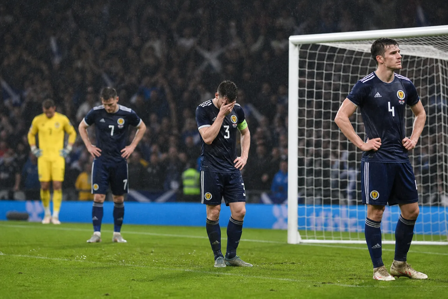 Fictional Scottish players reacting after a decisive qualification setback in the rain